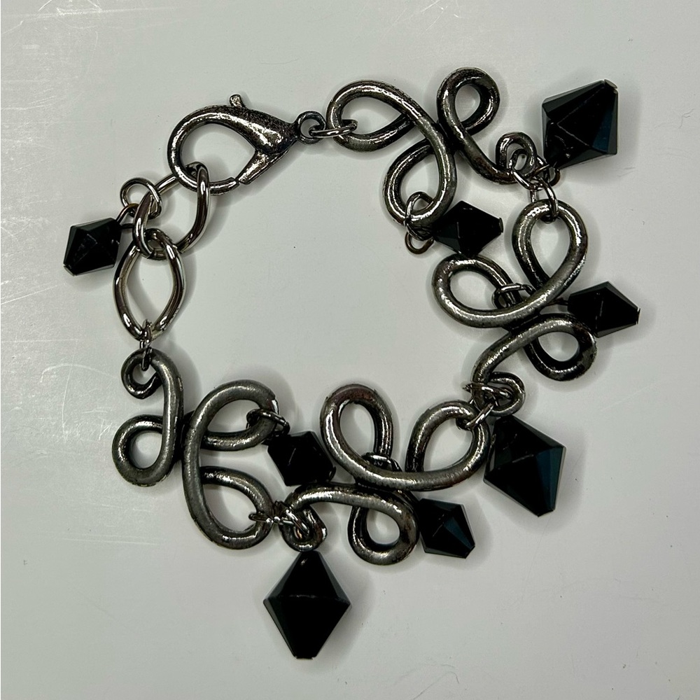 Faceted black dangling beads hang from brushed silver tone scroll link bracelet
